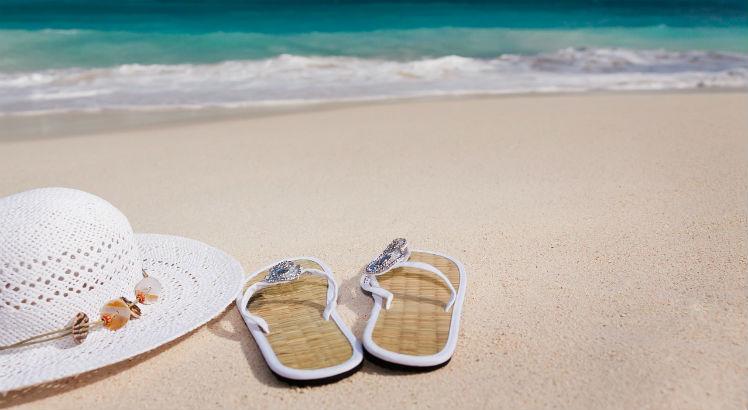 Imagem de chapéu e sandálias na areia da praia e mar ao fundo (Foto: Pixabay)