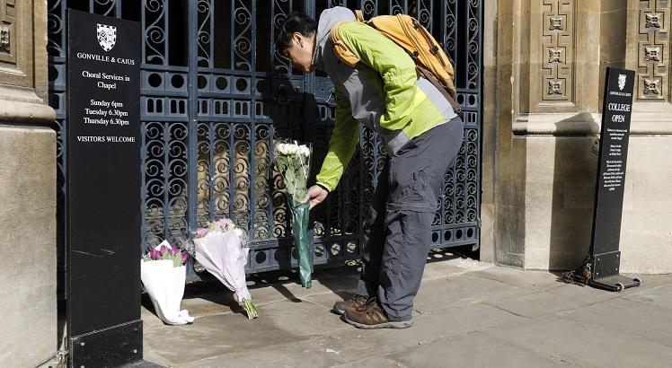 Um homem coloca flores no portão do Gonville and Caius College, na Universidade de Cambridge (AFP / Tolga AKMEN)