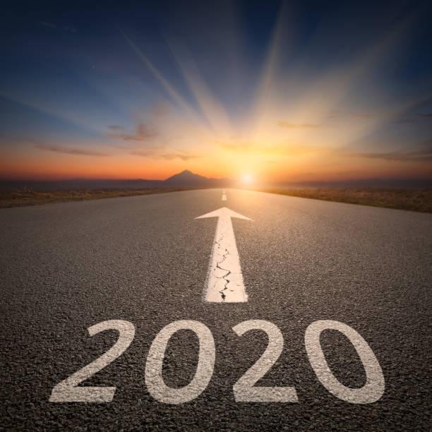 Upcoming 2020 new year on empty highway leading to the mountains through the desert against the rising sun.