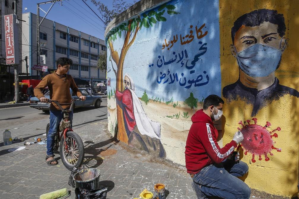 Artista palestino finaliza um mural com a frase: 'Combatendo a epidemia, nós protegemos o ser humano e preservamos a Terra', em Rafah, no sul da Faixa de Gaza — Foto: Mohammed Abed/AFP