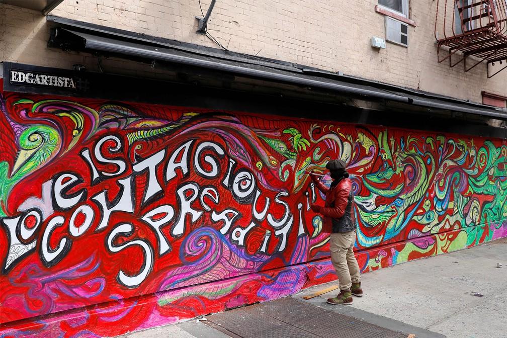 O artista e designer Edgartista dá retoques no seu mural que diz: 'O amor é conagiante. Espalhe-o', durante quarentena devida ao coronavírus, no Brooklyn, em Nova York — Foto: Andrew Kelly/Reuters