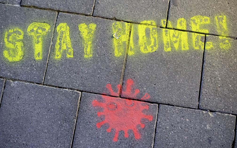'Fique em casa!', diz a frase em estêncil pintada com uma representação do coronavírus no chão de uma praça em Munique, na Alemanha — Foto: Sven Hoppe/DPA via AP