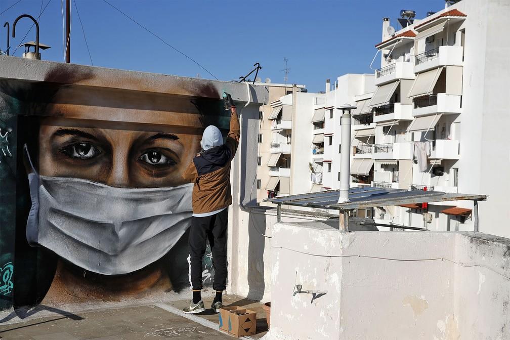 Um jovem grego de 16 anos de idade dá retoques no grafite de uma mulher usando uma máscara, inspirado na pandemia do coronavírus, no telhado do prédio onde ele mora em Atenas. Foto de terça-feira (17) — Foto: Thanassis Stavrakis/AP